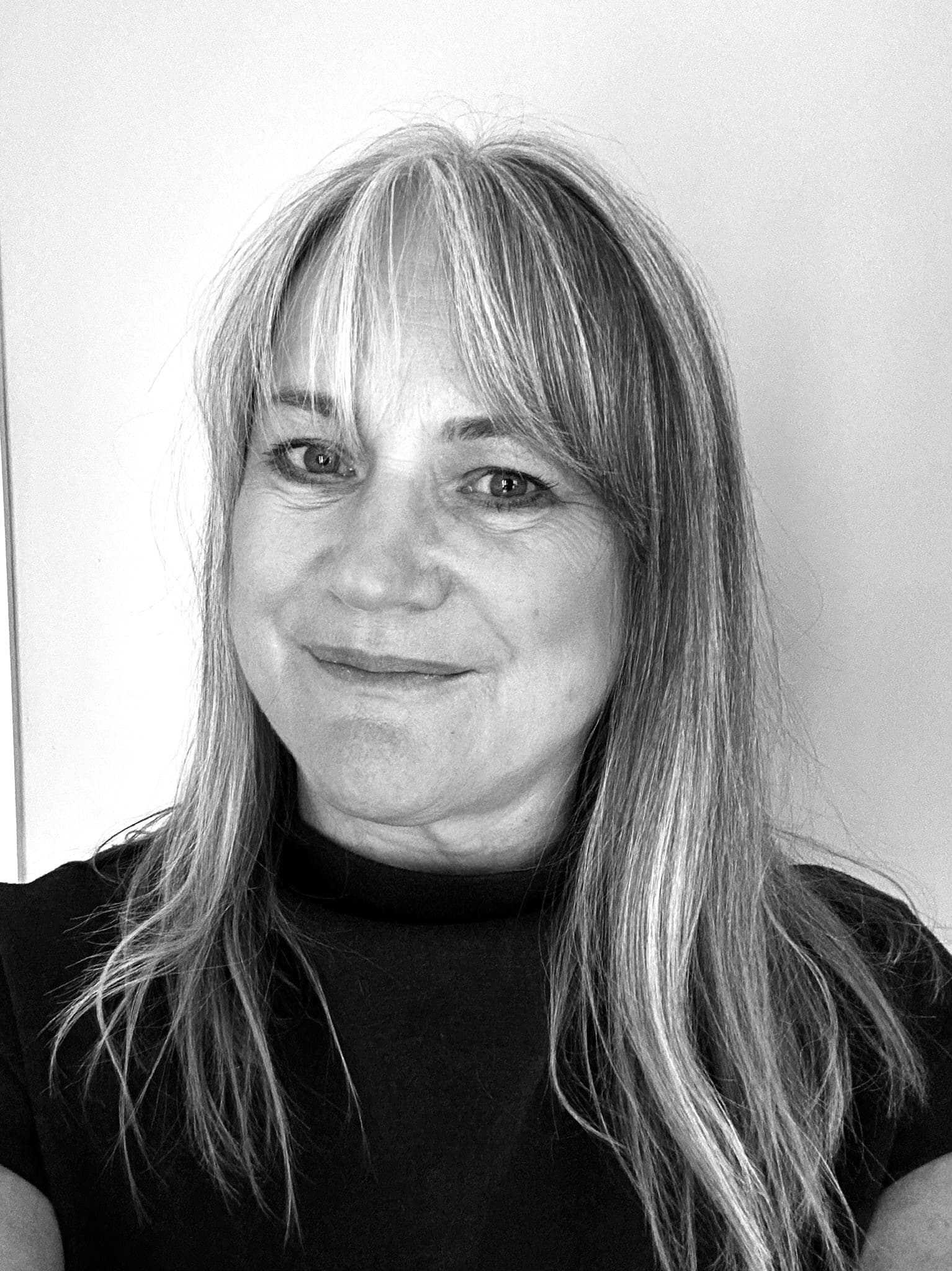 Black and white portrait of a woman with long, straight hair and bangs, smiling gently.